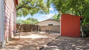A backyard with a covered patio area, a red shed, and a white building. - Brookswood #A xxxxxx (Austin)