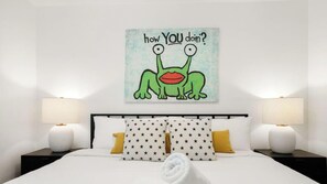 A hotel room with a bed, two nightstands, two lamps, and a wall with a cartoon character and text.