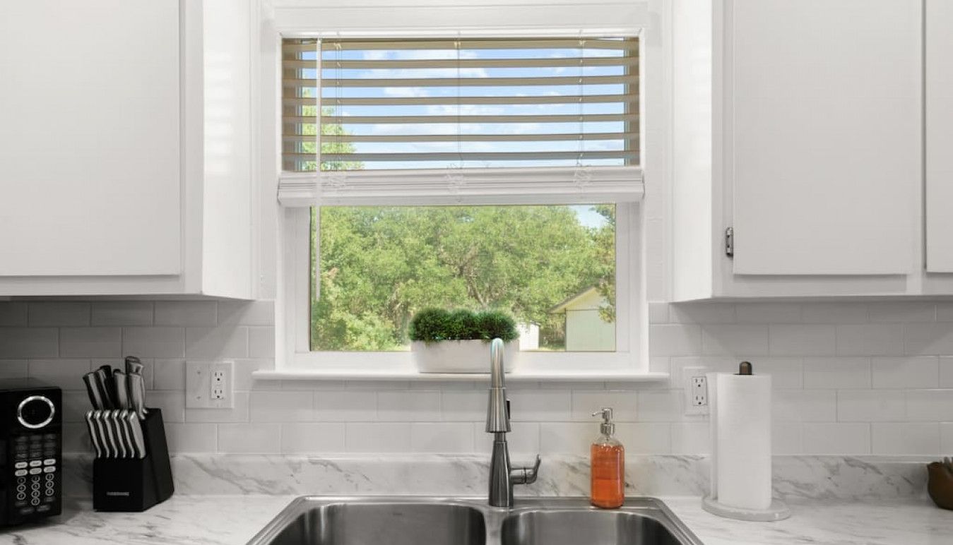 A kitchen with a double sink, a potted plant on the window sill, and a countertop with a soap dispenser.