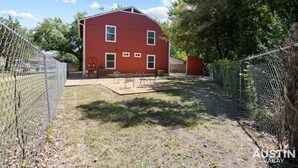 Un bâtiment rouge avec une cour entourée d’une clôture, une terrasse avec des chaises et un petit abri de jardin.