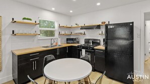 Une cuisine moderne avec des meubles noirs, un plan de travail blanc, un réfrigérateur noir et une table de salle à manger ronde.