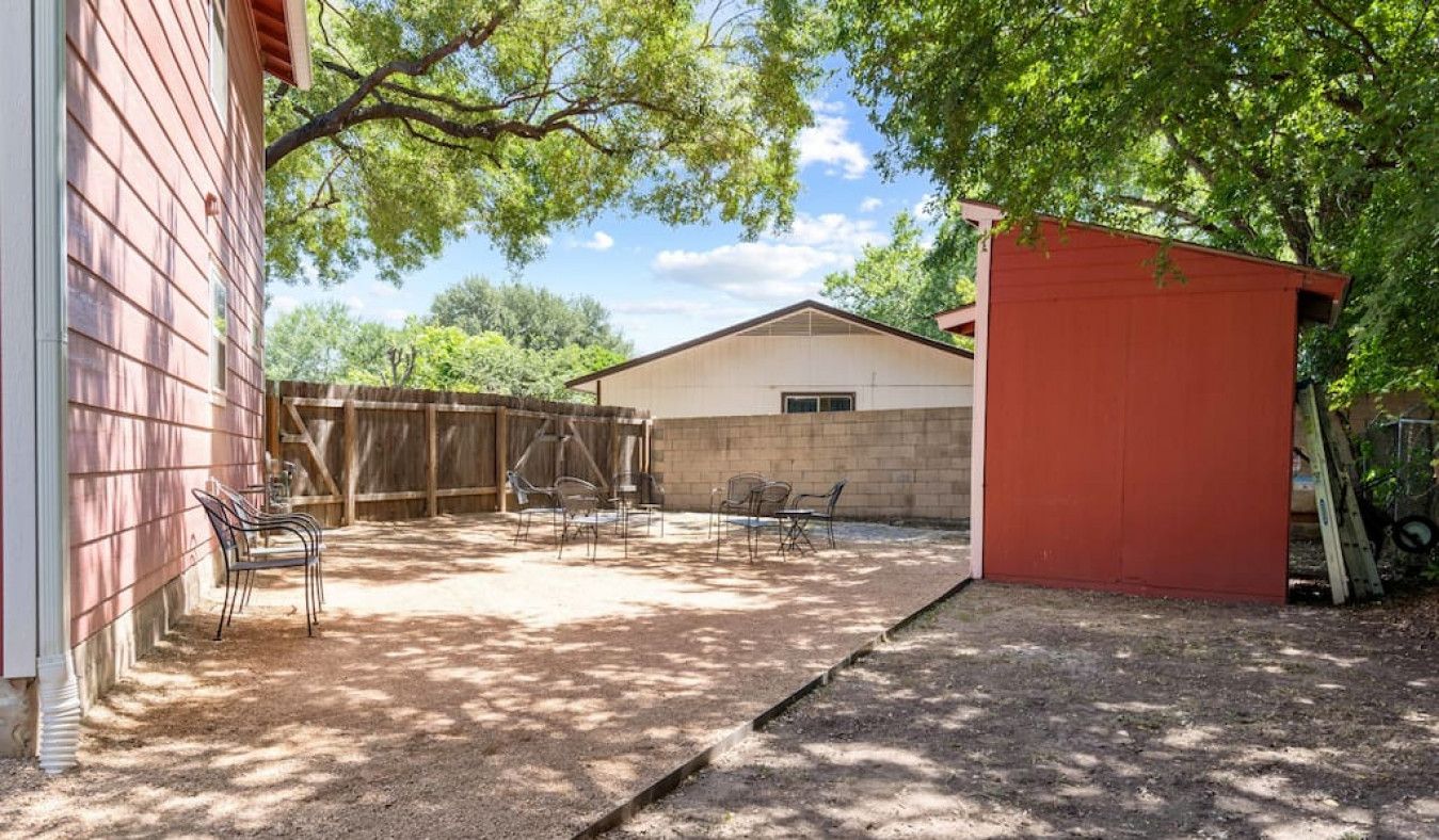 A backyard with a covered patio area, a red shed, and a white building.