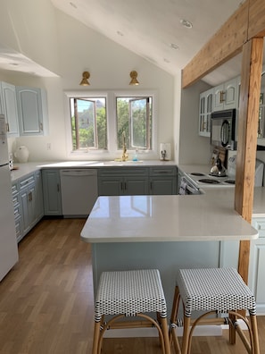 A modern kitchen with light blue cabinets, a white island, and two wicker bar stools.