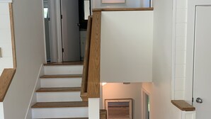 A staircase with wooden steps and white walls, leading to a landing with a framed picture and a small shelf. - Newly Renovated Quonnie Beach House -  QEBA Beach Pass & Pond Access (Charlestown)