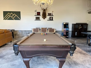 A pool table with a mounted deer head decoration, a sofa, and a chandelier.