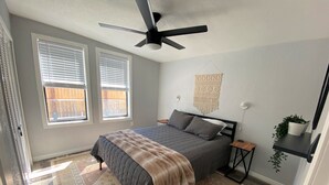 A bedroom with a bed, a ceiling fan, two windows, a wall-mounted macrame, a small side table, and a potted plant. - Explore like a local with access to everything Flagstaff has to offer (Flagstaff)