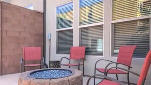A patio area with a stone fire pit and four chairs with red cushions.