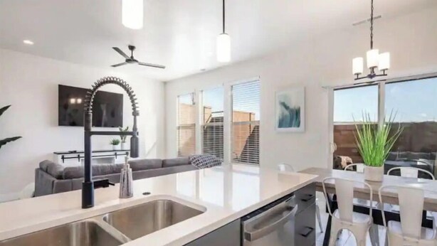 A modern kitchen with a dishwasher, double sink, and a dining area with white chairs and a table.