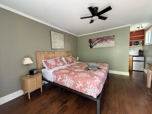 A bedroom with a bed, bedside table, lamp, ceiling fan, artwork, and a view of a kitchen area. - Old Town "Gem", Near Historic Downtown Saint Augustine (St. Augustine)