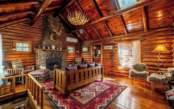 A log cabin interior with a stone fireplace, wooden furniture, and a red patterned rug. - Shell Town Cabin- Classis Log Cabin, Large Fireplace, Base of the Bighorns Location (Shell)
