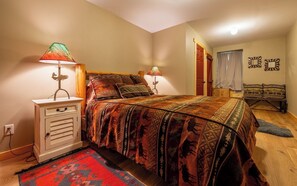 A bedroom with a bed, two bedside lamps, a nightstand, a bench, and a door. - Shell Town Cabin- Classis Log Cabin, Large Fireplace, Base of the Bighorns Location (Shell)