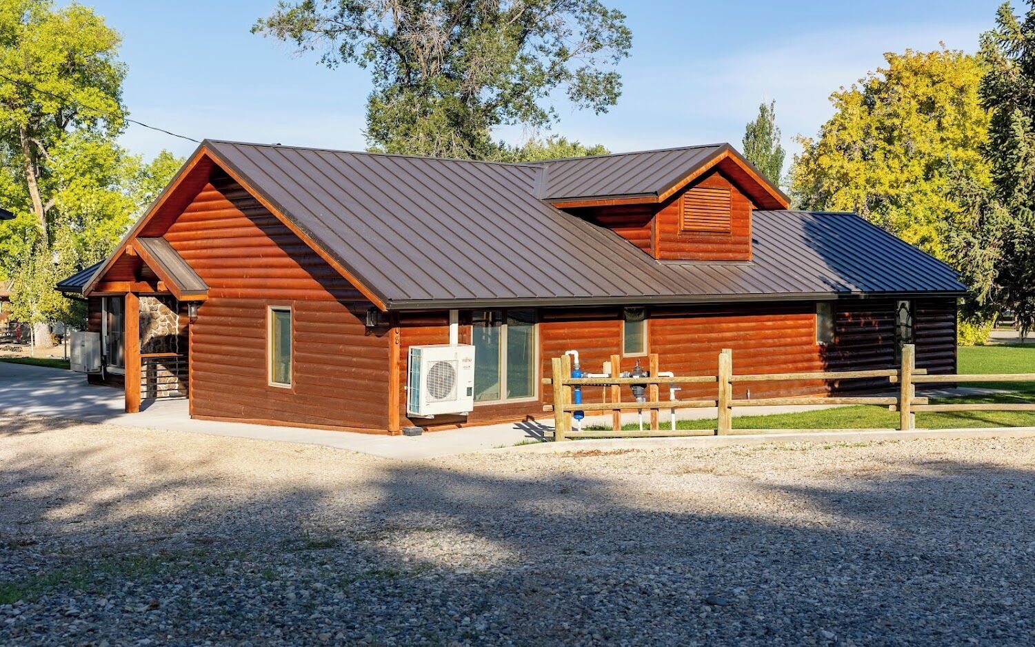 A wooden cabin with a metal roof, a gravel driveway, and a wooden fence.