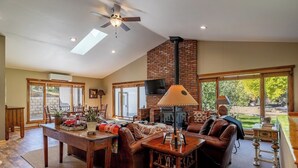 A spacious living room with a fireplace, a ceiling fan, and large windows offering a view of the outdoors. - Great Shell Wyoming Escape- Large Family Retreat at the Base of the Bighorn Mountains (Shell)