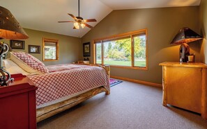 A bedroom with a bed, a wooden nightstand, a ceiling fan, and a window with a view of greenery.