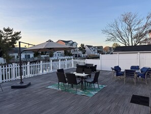 Een houten terras met een tafel en stoelen, een witte schutting en huizen op de achtergrond.