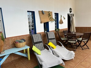 A sunlit patio area with two lounge chairs, a small table, and a dining table with chairs.