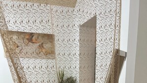 Une pièce avec un mur orné d’un motif géométrique, une chaise en osier et un tapis à motifs.