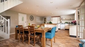 Un comedor con mesa y sillas de madera, una cocina al fondo y una escalera que sube a otro nivel.