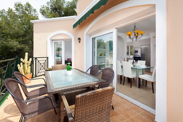 An outdoor dining area with wicker furniture, a glass table, and a cactus plant.