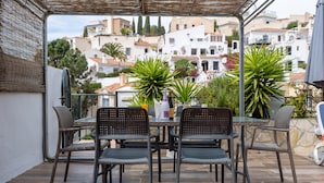 Eine Außenpatio mit Tisch und Stühlen, umgeben von Kübelpflanzen, mit Blick auf eine Hügelkuppe und Gebäude.