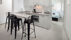 Eine moderne Küche mit einer zentralen Kochinsel, Barhocker und Blick in ein Schlafzimmer.