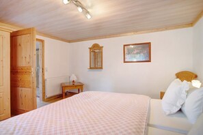 Une chambre à coucher avec un lit, une armoire en bois, une table de chevet avec une lampe, un tableau encadré au mur et un radiateur.
