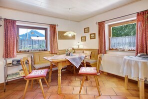 A dining area with a table, chairs, a bench, a radiator, and a window with curtains.