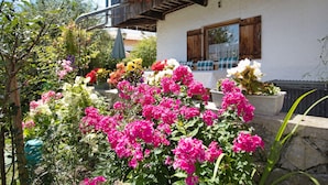 A garden with various flowers in front of a building with a balcony. - Apartment 'Löwenzahn' with Mountain View, Terrace & Wi-Fi (Fischbachau)