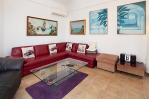 A living room with a red sofa, a glass coffee table, a beige armchair, and a small wooden side table with speakers. - Villa Miramar Burriana Beach 6 pax with Sea Views & Pool (Nerja)