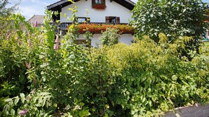Un chalet tradizionale con un balcone, immerso nel verde e circondato da piante fiorite.