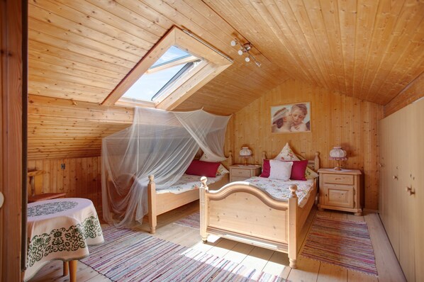 A bedroom with a sloped ceiling, a bed with a canopy, bedside tables, and a small table with a tablecloth.