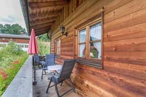 A wooden cabin with a deck, a table, and two chairs. - Apartment 'Edelweiß' with Mountain View, Balcony and Wi-Fi (Fischbachau)