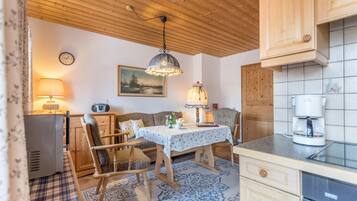 Une cuisine chaleureuse avec des meubles en bois, une table à manger, des chaises, une machine à café et une horloge au mur.
