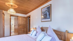 A bedroom with a wooden ceiling, a bed with checkered bedding, a nightstand with a lamp, and a framed picture on the wall. - Apartment 'Enzian' with Mountain View, Balcony and Wi-Fi (Fischbachau)