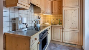 A kitchen with wooden cabinets, a stove, a coffee maker, and a sink. - Apartment 'Enzian' with Mountain View, Balcony and Wi-Fi (Fischbachau)