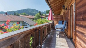 A wooden balcony with a table and chairs, overlooking a village and hills. - Apartment 'Enzian' with Mountain View, Balcony and Wi-Fi (Fischbachau)