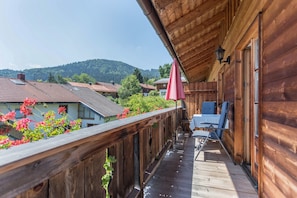 Un balcon en bois, agrĂ©mentĂ© dâune table et de chaises, qui offre une vue sur un village et des collines.