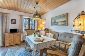 Una habitación acogedora con techo de madera, una mesa de comedor con mantel floral, un sofá y una lámpara.