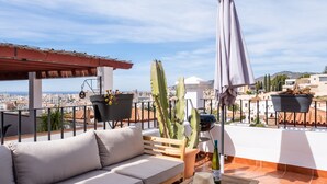 Une terrasse sur le toit, avec un canapé, une table sur laquelle sont posés un chapeau et des lunettes de soleil, un barbecue et des plantes en pot.