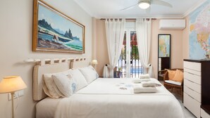 Une chambre d’hôtel comprenant un lit, une table de chevet, une lampe, une chaise, une commode, un tableau et une fenêtre avec des rideaux.