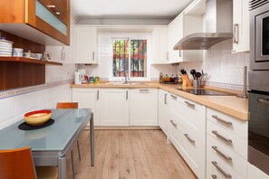 Cozinha moderna com armários brancos, uma mesa de vidro e uma janela com vista para o verde.
