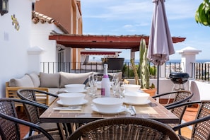 Um terraço com mesa de jantar para quatro pessoas, mobiliário para área externa, churrasqueira e vista da cidade.