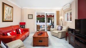 Un salon avec un canapé rouge, un canapé beige, une table basse en bois, un téléviseur et une porte-fenêtre coulissante donnant sur un espace extérieur.