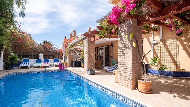 Une piscine avec des chaises longues, une pergola ornée de fleurs et un bâtiment en briques.