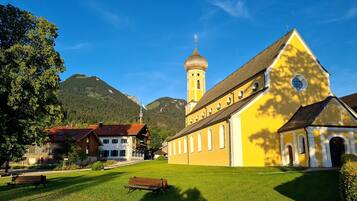 Eine Kirche mit einem Glockenturm, einem Rasenhof und einem Berg im Hintergrund.