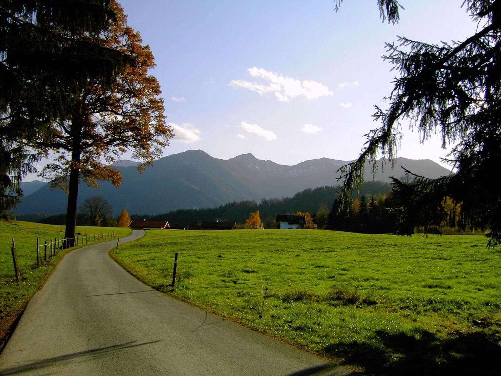 A rural road curving through a green field with mountains in the background.
