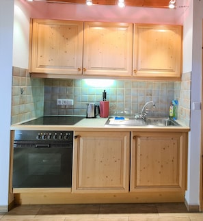 Una cocina con armarios de madera, una estufa negra, un fregadero y un salpicadero de azulejos.