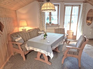 A cozy room with a wooden ceiling, a sofa, a table with a checkered tablecloth, and a chair.
