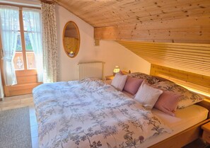 A bedroom with a wooden ceiling, a bed with floral bedding, a bedside lamp, and a window with curtains.