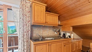 Cocina de cabaña de madera con encimera de madera, un lavamanos, armarios y una ventana con cortinas.